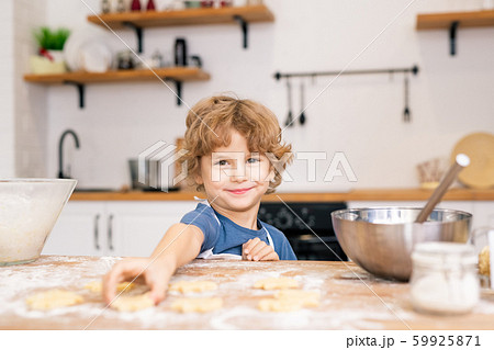 Smiling little boy looking at you while going to take cookie on table Smiling little boy looking at you while going to take cookie on table 59925871