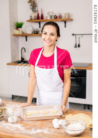 Young cheerful woman in apron looking at you while preparing tasty cookies Young cheerful woman in apron looking at you while preparing tasty cookies 59926178