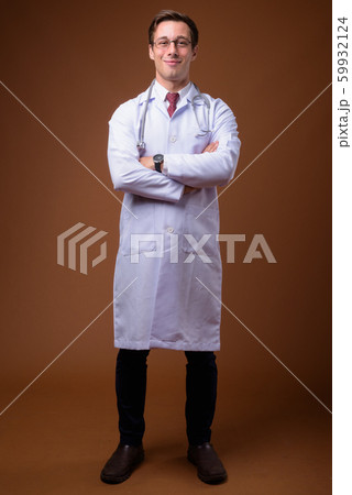 Young handsome man doctor against brown background Young handsome man doctor against brown background 59932124