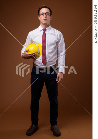 Young handsome businessman with hardhat against brown background 59932294