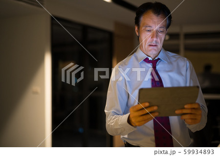 Mature Businessman In Office At Night Using Digital Tablet Computer Mature Businessman In Office At Night Using Digital Tablet Computer 59934893