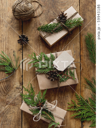 Christmas presents wrapped in craft paper with natural fir tree and thuja branches as decoration. Top view on wooden table with hand made New Year gifts. 59943186