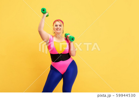 Young caucasian plus size female model's training on yellow background Young caucasian plus size female model's training on yellow background 59944530