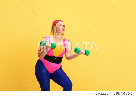Young caucasian plus size female model's training on yellow background Young caucasian plus size female model's training on yellow background 59944550