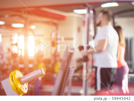 A man and a girl are engaged in a modern gym against the backdrop of sunny sunset, blurred, background A man and a girl are engaged in a modern gym against the backdrop of sunny sunset, blurred, background 59945042