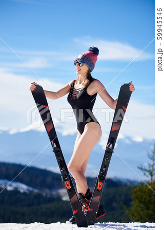 Sexy young woman holding skis in black swimsuit and sunglasses on background of mountain landscape. 59945546