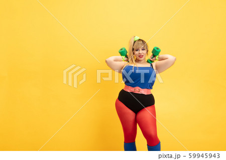 Young caucasian plus size female model's training on yellow background Young caucasian plus size female model's training on yellow background 59945943