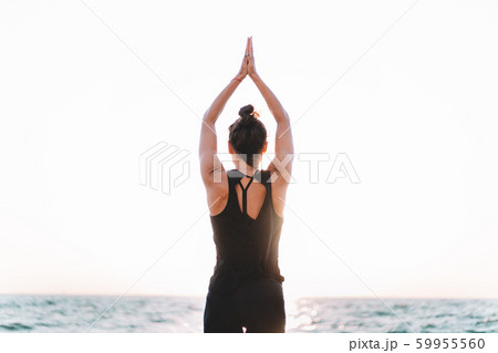 Slim woman in black bodysuit practicing yoga near sea or ocean during sunrise light. Flexibility, stretching, fitness, healthy lifestyle.  59955560