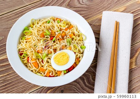 Instant noodles with egg and vegetables in white bowl and chopsticks on table napkin 59960113