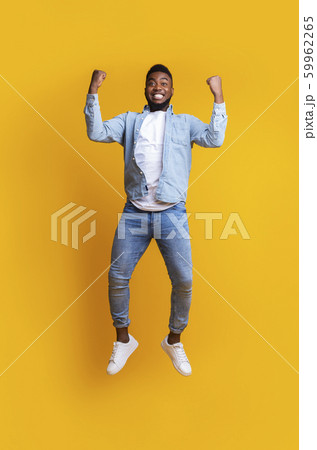 Euphoric afro guy jumping in air, celebrating success over yellow background 59962265