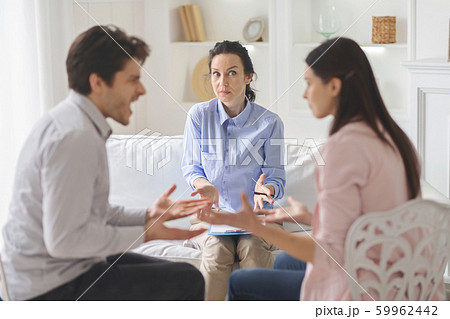 Confused psychologist watching young couple arguing in her office Confused psychologist watching young couple arguing in her office 59962442