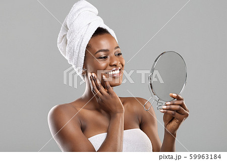 Beautiful african woman holding mirror and touching her perfect soft skin Beautiful african woman holding mirror and touching her perfect soft skin 59963184