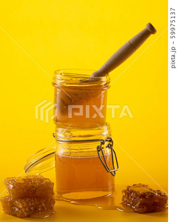 Two jars of honey with honeycombs and a stick on a yellow background Two jars of honey with honeycombs and a stick on a yellow background 59975137