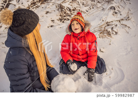 Happy family in warm clothing. Smiling mother and son making a snowman outdoor. The concept of Happy family in warm clothing. Smiling mother and son making a snowman outdoor. The concept of 59982987