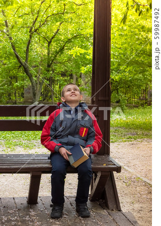Happy smiling boy sitting on bench with book Happy smiling boy sitting on bench with book 59987492