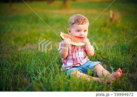Happy child sitting on green grass and eating watermelon outdoors in spring park against natural background 59994672