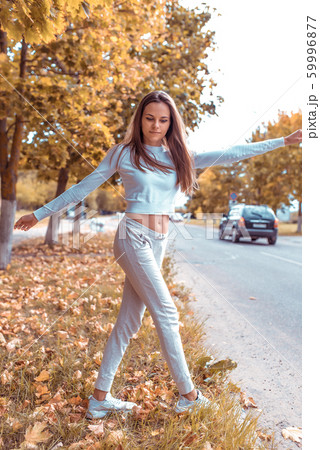 Beautiful girl in autumn on nature walks in grass, background trees fallen leaves, road car. Warm casual wear. Emotions of comfort of relaxation pleasure in nature. Long hair casual makeup. 59996877
