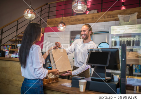 Dark-haired businesswoman talking to smiling cashier in the coffee shop Dark-haired businesswoman talking to smiling cashier in the coffee shop 59999230