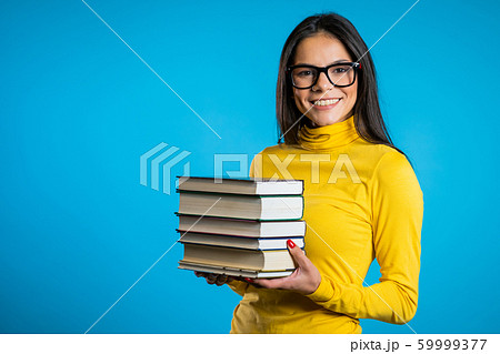 Latin student on blue background in the studio holds stack of university books from library. Guy smiles, he is happy to graduate. Copy space. 59999377