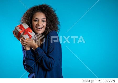 Pretty woman received gift box and interested in what's inside. Copy space. She is happy and flattered by attention. Girl on blue background. Studio picture. Pretty woman received gift box and interested in what's inside. Copy space. She is happy and flattered by attention. Girl on blue background. Studio picture. 60002779