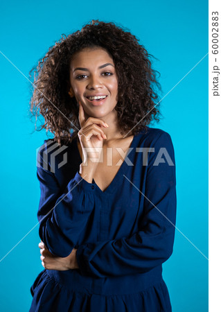 Attractive african american woman with afro hair in business clothing smiling to camera over blue wall background. Cute mixed race girl's portrait 60002883