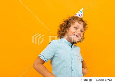 Smiling red-haired curly boy with a celebratory cap isolated yellow background Smiling red-haired curly boy with a celebratory cap isolated yellow background 60003798
