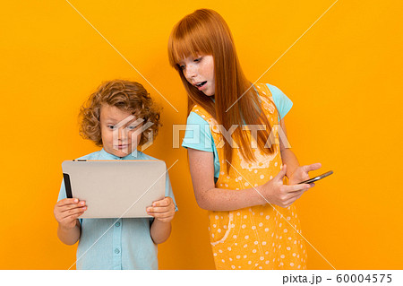Red-haired surprised boy and girl with a phone and a tablet on a yellow bright background 60004575