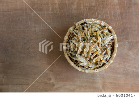 top view of raw dried little fish in a bamboo basket on wooden table. top view of raw dried little fish in a bamboo basket on wooden table. 60010417