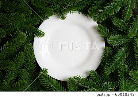 Top view of white plate surrounded with fir tree 60018245
