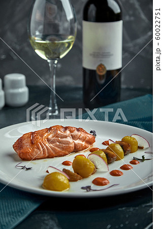 A large roasted piece of red fish lies on a white plate with vegetables, a beautiful serve in a restaurant 60022751