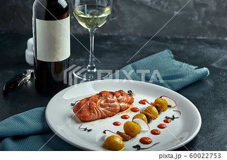 A large roasted piece of red fish lies on a white plate with vegetables, a beautiful serve in a restaurant A large roasted piece of red fish lies on a white plate with vegetables, a beautiful serve in a restaurant 60022753