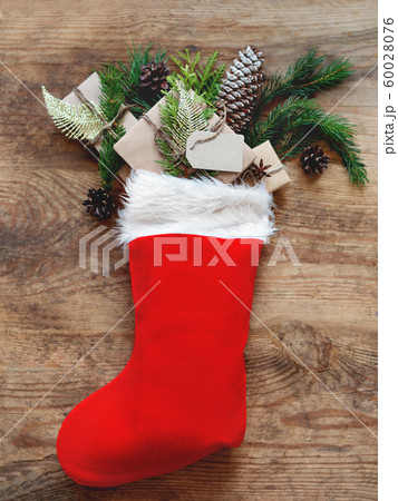 Christmas presents in Santa Claus red sock. Gifts in craft paper with fir tree branches and clear tag on wooden background. 60028076
