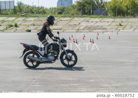 Girl with red hair and in dome learning to ride a bike at motorcycle racing track. Biker on a motorcycle. 60028752