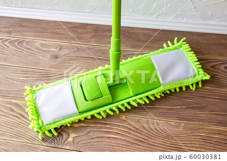 Green plastic mop on a brown wooden floor. Wash the floor. Housekeeping and household chores. 60030381