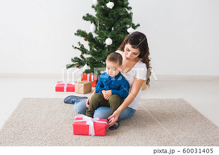 Christmas, single parent and holidays concept - Cute little boy holding christmas present for his mother at the home. Christmas, single parent and holidays concept - Cute little boy holding christmas present for his mother at the home. 60031405