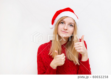 Cheerful woman in santa hat showing thumb up. Girl looking at camera and smiling isolated on white background. 60032258