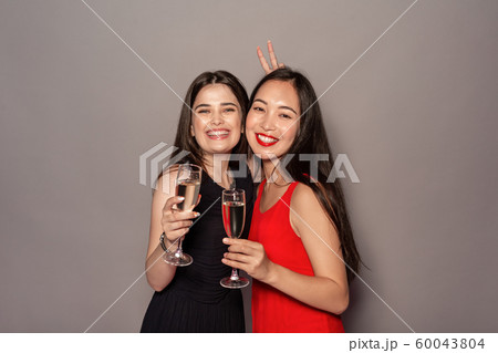 Freestyle. Young girls in dresses standing isolated on gray with glasses of champagne posing to Freestyle. Young girls in dresses standing isolated on gray with glasses of champagne posing to 60043804
