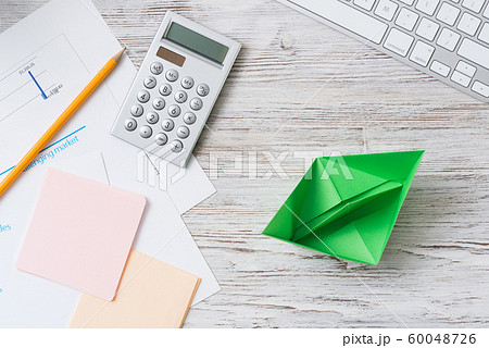 Top view office workspace with green paper ship 60048726