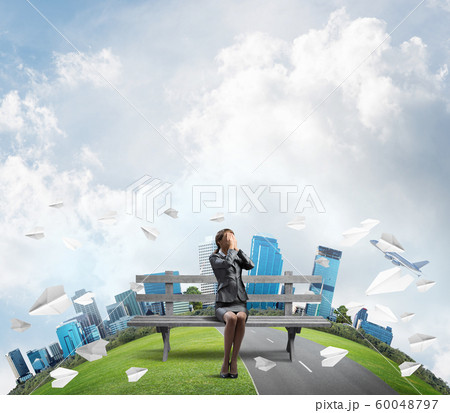 Young woman sitting on wooden bench outdoors 60048797