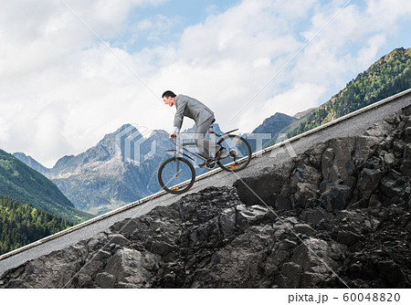 Businessman riding downhill by bike Businessman riding downhill by bike 60048820