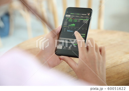 Female hand with smartphone trading stock online in coffee shop , Business concept 60051622
