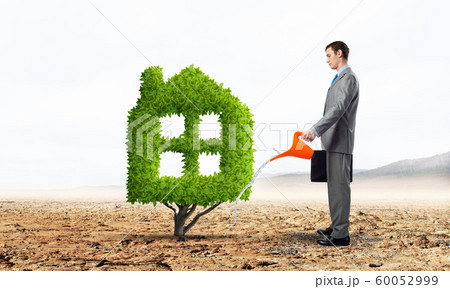 Businessman watering green plant in shape of house Businessman watering green plant in shape of house 60052999