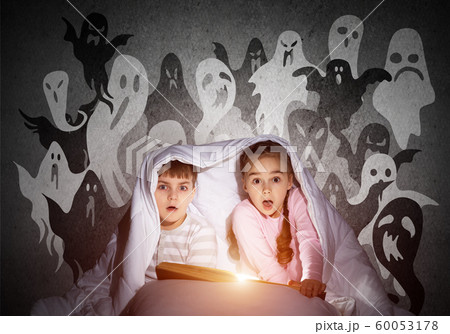 Scared girl and boy reading book in bed 60053178