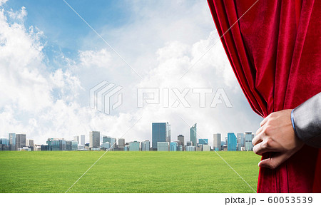 Green meadow behind red curtain and hand holding it Green meadow behind red curtain and hand holding it 60053539