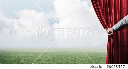 Green meadow behind red curtain and hand holding it 60053567