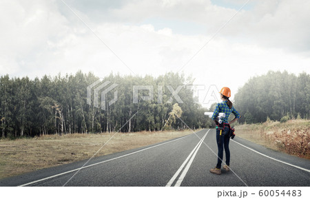 Young woman in safety helmet standing on road Young woman in safety helmet standing on road 60054483
