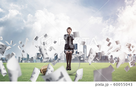 Young woman sitting on light bulb on green meadow 60055043