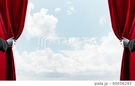 Cloudy landscape behind red curtain and hand holding it Cloudy landscape behind red curtain and hand holding it 60056293