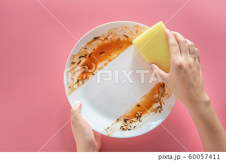 woman using yellow cleaning sponge to clean up and washing food stains and dirt on white dish after eating meal isolated on pink background. cleaning , healthcare and sanitation at home concept woman using yellow cleaning sponge to clean up and washing food stains and dirt on white dish after eating meal isolated on pink background. cleaning , healthcare and sanitation at home concept 60057411