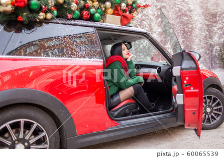 Pretty young girl is sitting in red car with decorated xmas tree on the roof. Pretty young girl is sitting in red car with decorated xmas tree on the roof. 60065539